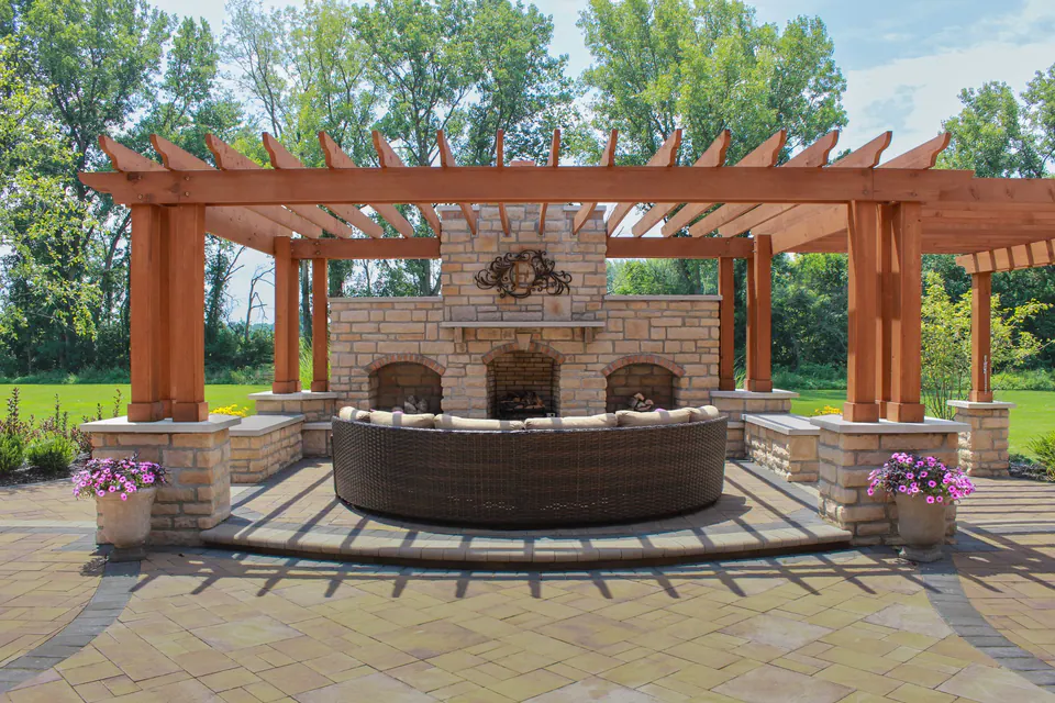 Timber pergola and limestone outdoor fireplace with stone column bases, paver patio, and lounge seating